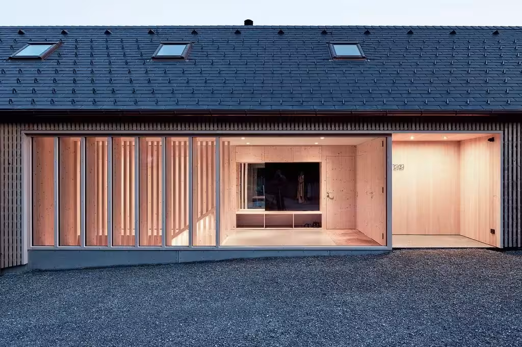 Fachada de la Casa de Julia y Björn al anochecer con tejado oscuro, lamas de madera y un porche iluminado
