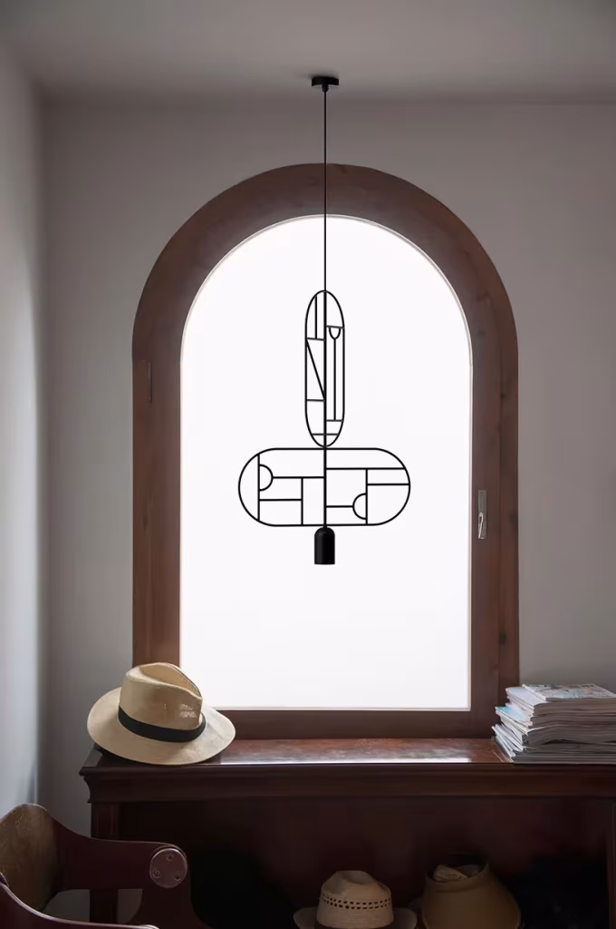 Lámpara colgante de varilla negra ante una ventana en arco con un sombrero sobre un mueble de madera