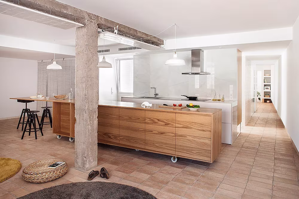 Isla de cocina de madera sobre ruedas con taburetes negros y suelo de barro cocido en L'Àtic Vernacle