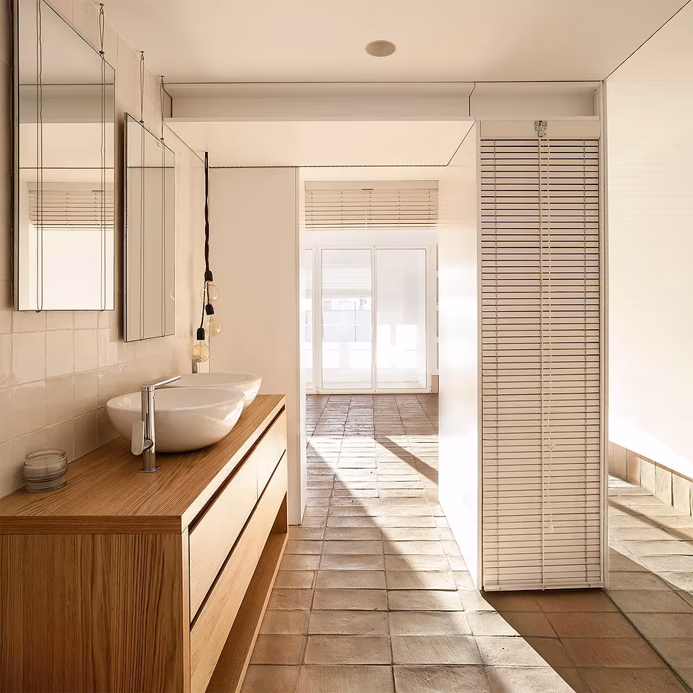 Baño de L'Àtic Vernacle con mueble de madera, lavabo de cuenco blanco y persianas de lamas