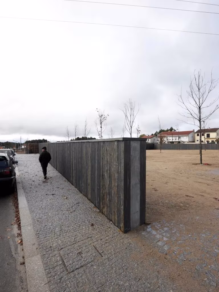 Muro de madera oscura del Espacio Miguel Torga junto a una acera de adoquines con una persona caminando
