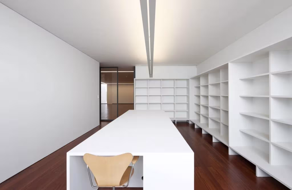 Biblioteca del Espacio Miguel Torga con mesa blanca alargada, estanterías blancas y suelo de madera