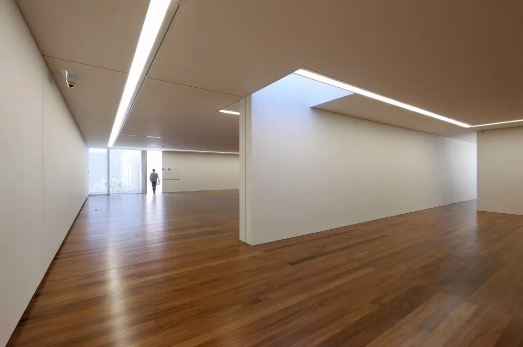 Sala blanca del Espacio Miguel Torga con suelo de madera brillante y una línea de luz en el techo