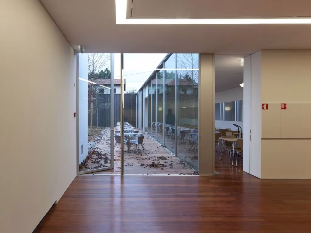 Vestíbulo del Espacio Miguel Torga con suelo de madera y fachada de vidrio hacia un patio con mesas