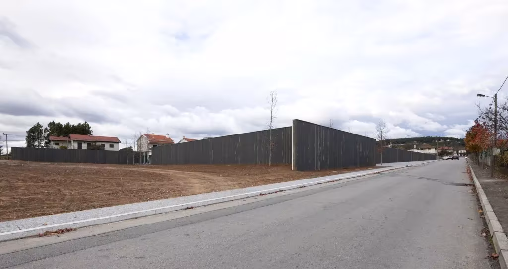 Carretera junto al largo muro de madera negra del Espacio Miguel Torga bajo un cielo nublado
