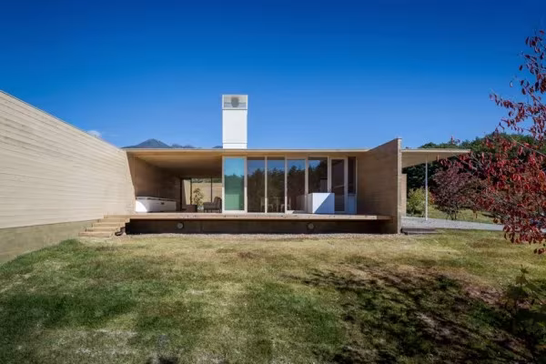 Solid Cedar House de Shigeru Ban con cubierta plana, chimenea blanca y fachada acristalada sobre el césped