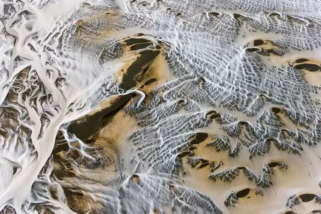 Vista aérea de un paisaje de nieve y tierra ocre surcado por cauces que dibujan formas ramificadas