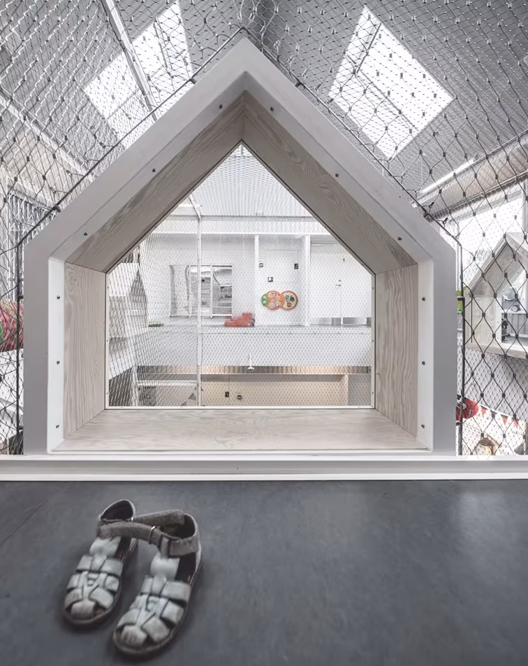 Hueco con forma de casa en un muro interior blanco de la guardería, con unas sandalias infantiles delante