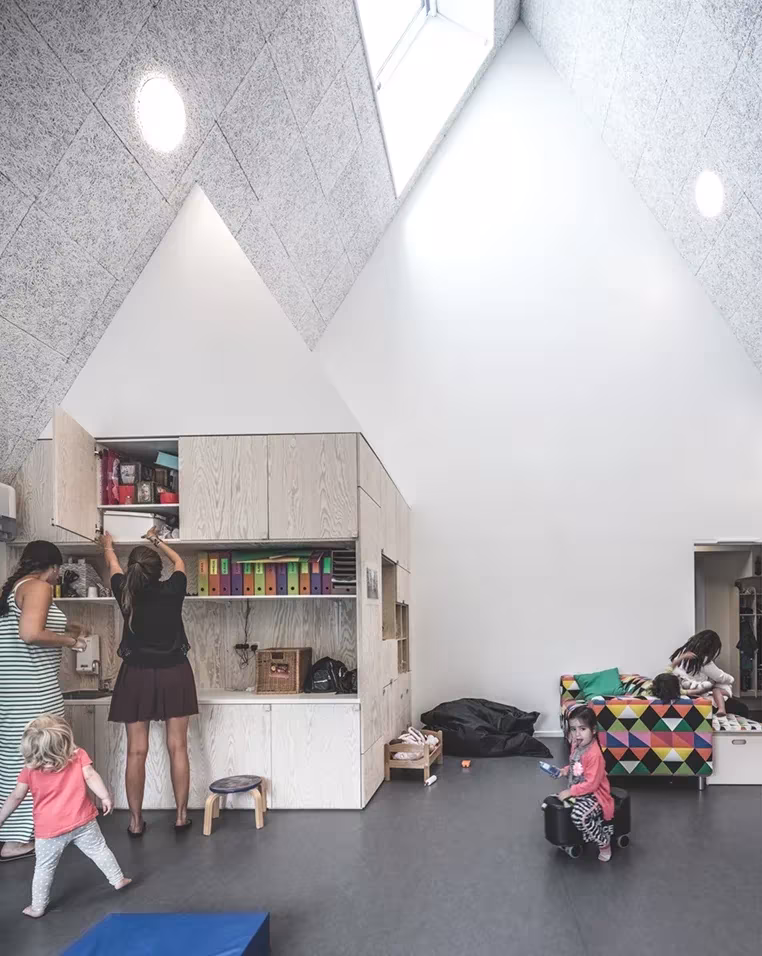 Aula de techo inclinado de la guardería Frederiksvej con muebles de madera clara y niños jugando