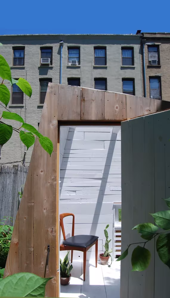 Puerta abierta del estudio de cedro de Nicholas Hunt en un patio de Brooklyn con una silla dentro