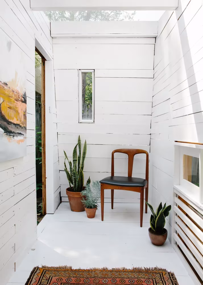 Interior blanco del Brooklyn Garden Studio con silla de madera, plantas en macetas y alfombra