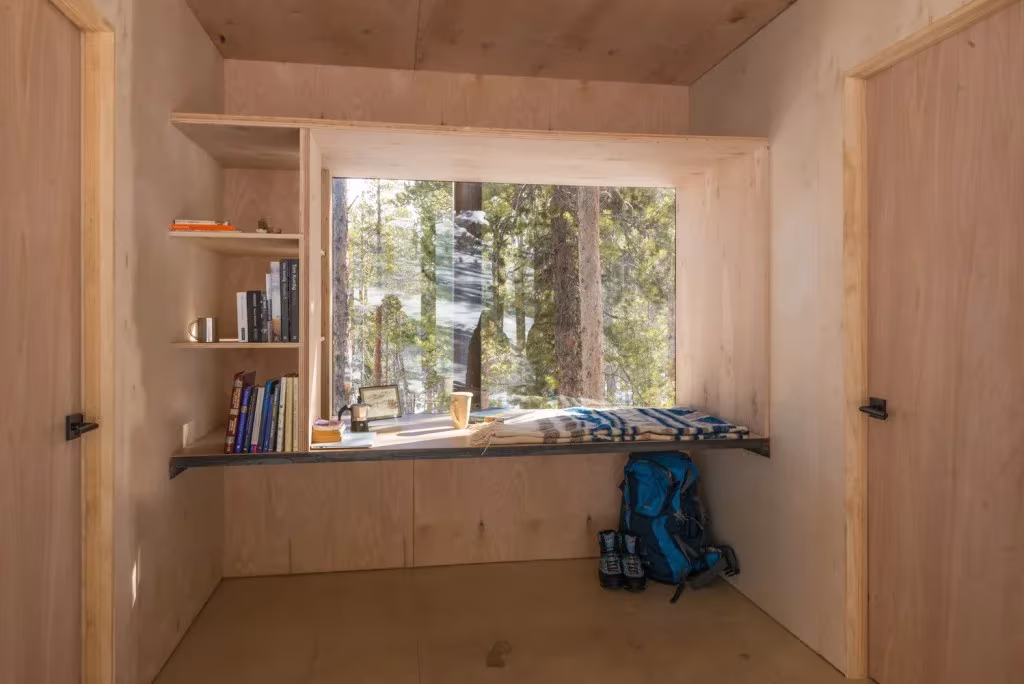 Interior de madera de una cabaña de Colorado Outward Bound con estantería, banco y ventana al pinar