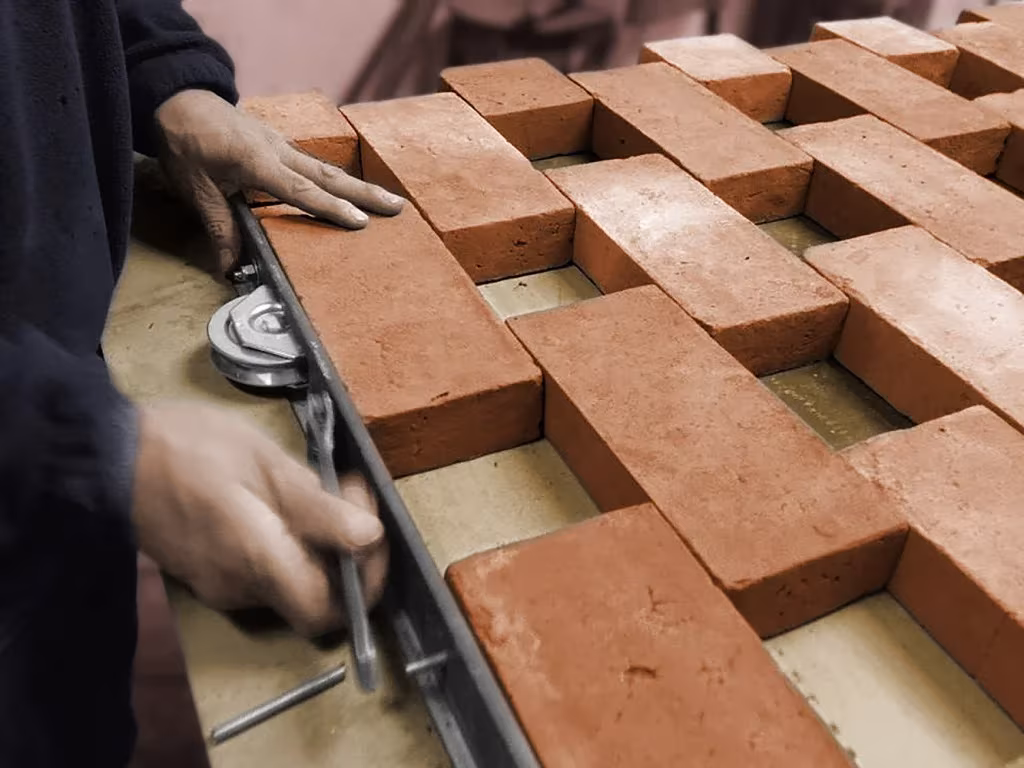 Manos montando ladrillos macizos en un bastidor metálico para formar la celosía ajedrezada