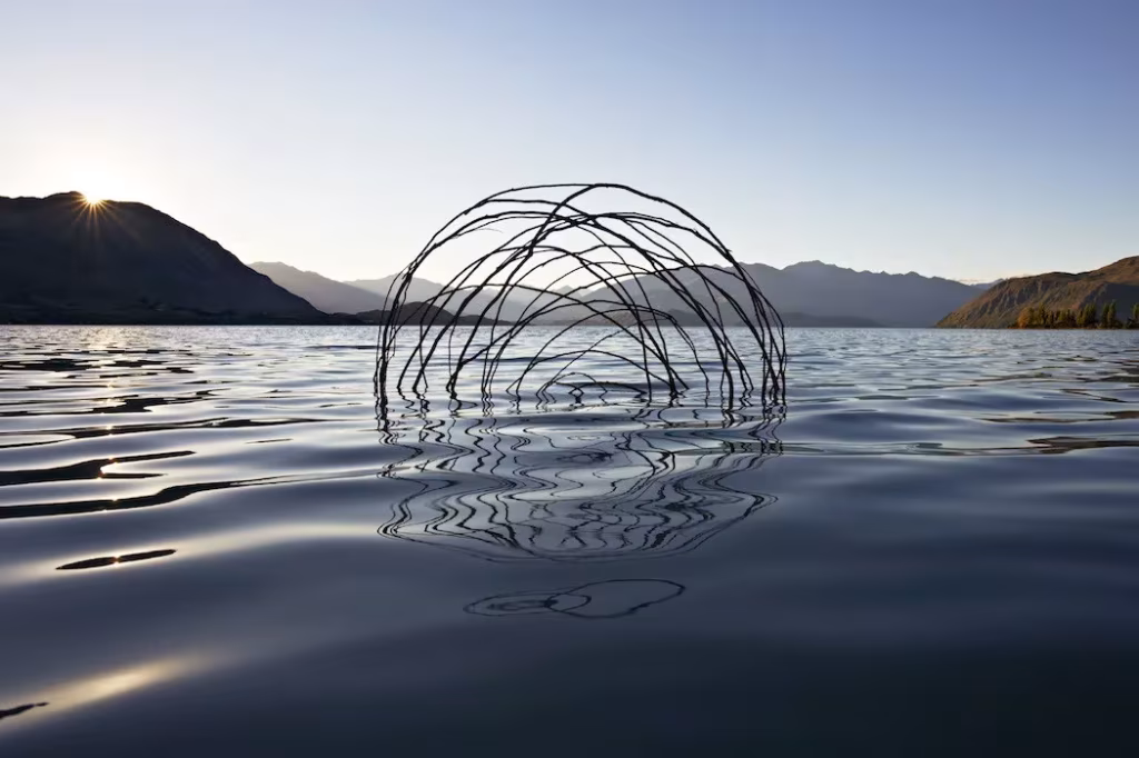 Escultura de círculos entrelazados de Martin Hill sobre la superficie de un lago entre montañas