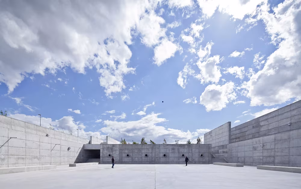 Gran explanada del Parque Venecia rodeada de muros de hormigón con paseantes bajo un cielo de nubes