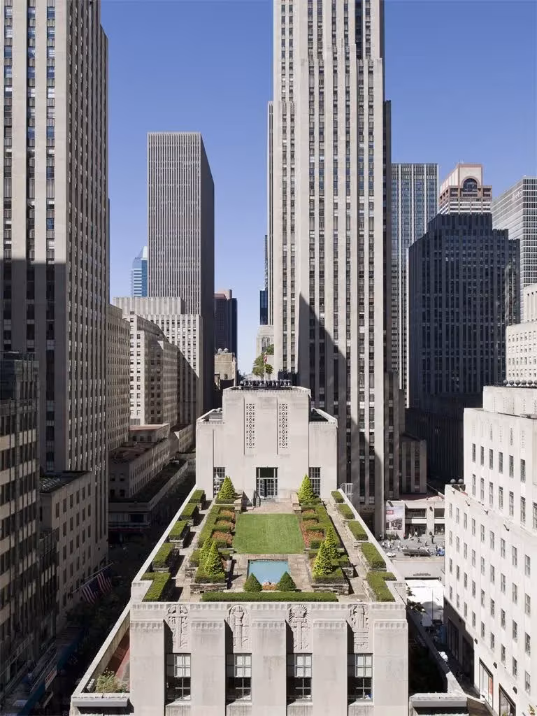 Cubierta ajardinada del Rockefeller Center con setos y estanque entre rascacielos de Nueva York