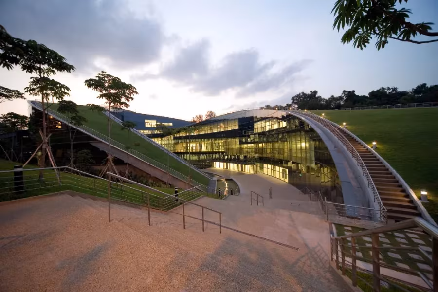 Cubiertas vegetales curvas de la Universidad Tecnológica de Nanyang al atardecer, con edificios acristalados iluminados
