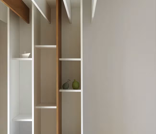 Estantería abierta blanca con montantes de madera en la Casa BHMM, con frutas sobre un estante