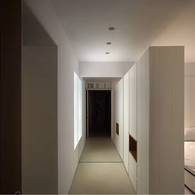 Pasillo blanco de la Casa BHMM con hueco iluminado y armarios con nicho de madera