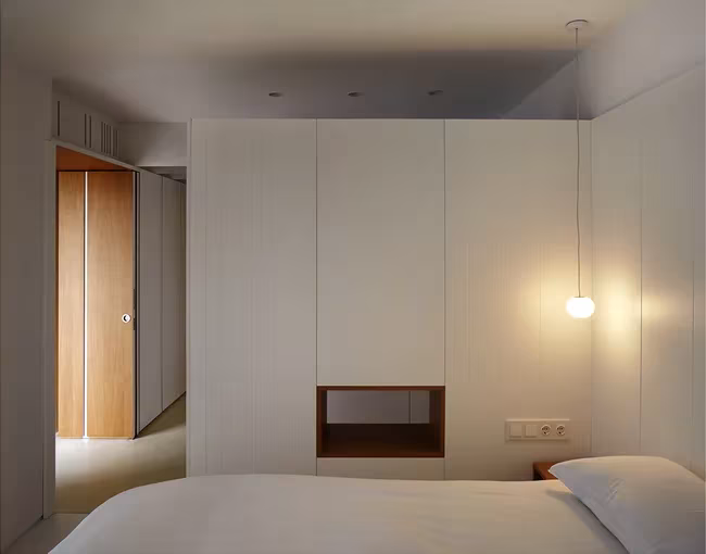 Dormitorio de la Casa BHMM con cama blanca, lámpara colgante y pieza de armarios con nicho de madera