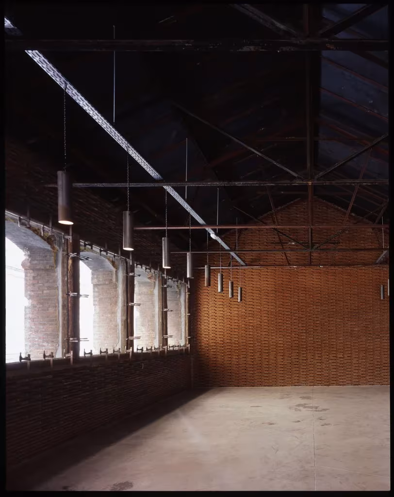 Sala de la nave 8B del Matadero con cubierta de cerchas, ventanas altas y muro de ladrillo al fondo