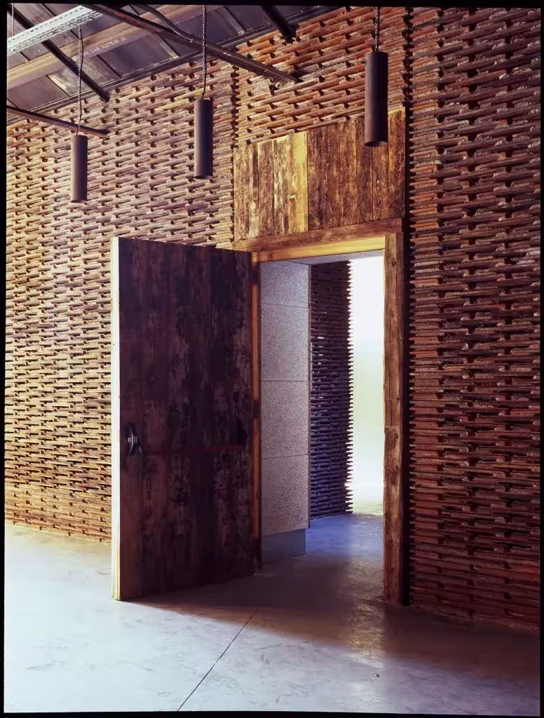 Puerta de madera pivotante abierta en un muro de tejas recuperadas en la nave 8B del Matadero