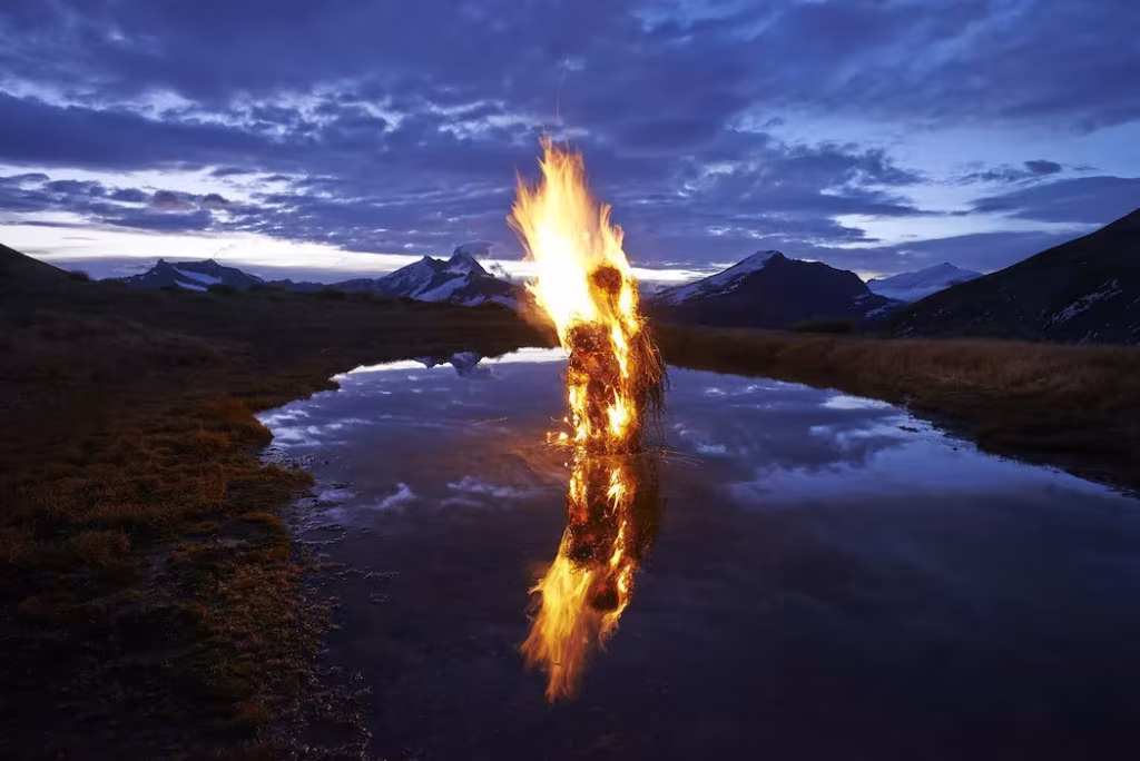 Escultura en llamas de Martin Hill reflejada en un lago de montaña al anochecer