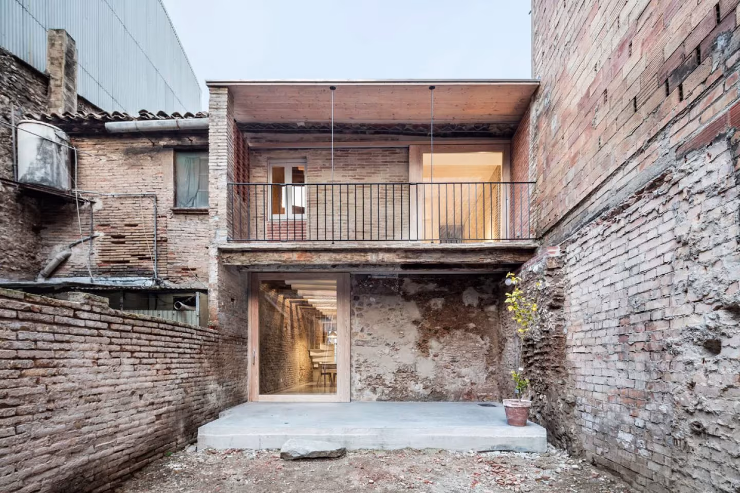 Patio de la casa entre medianeras de DataAE antes de la reforma, con muros de ladrillo y balcón nuevo, Sant Feliu