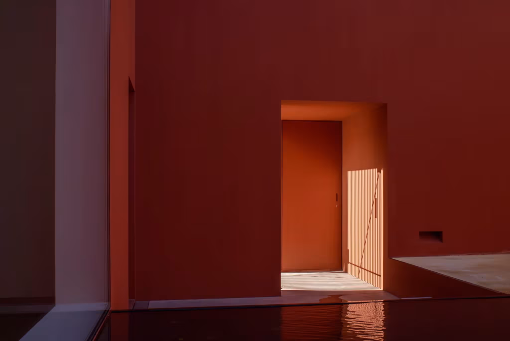 Muros rojos y una lámina de agua reflejando la luz en el patio de la Casa en Oeiras