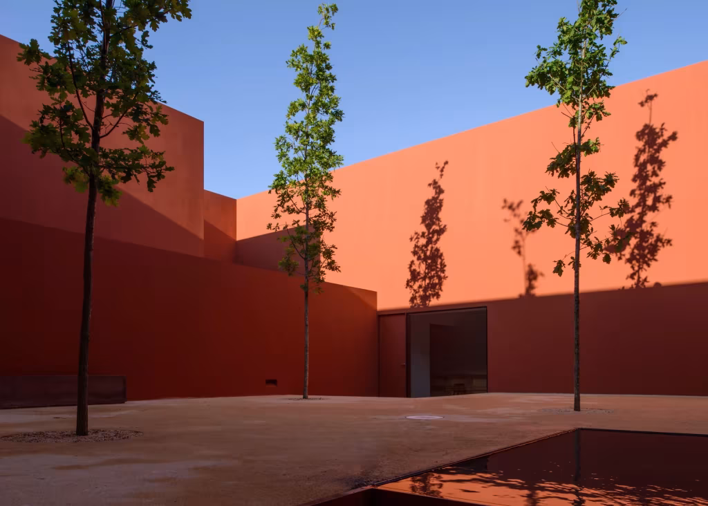 Patio de muros rojos con árboles esbeltos y estanque bajo cielo azul en la Casa en Oeiras