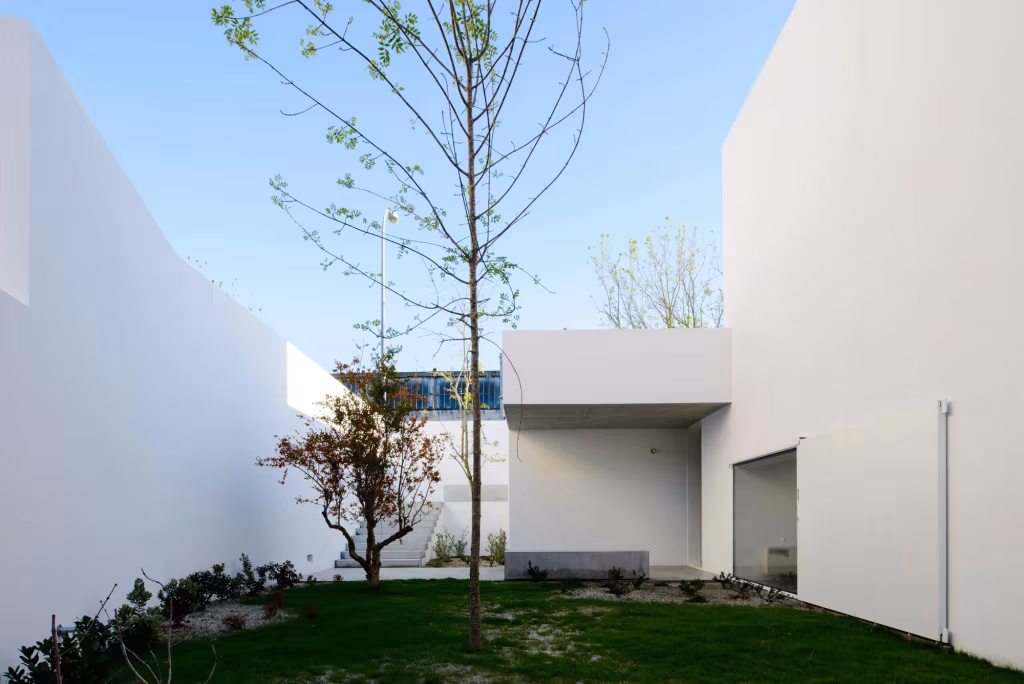 Jardín con césped y árboles jóvenes entre los muros blancos de la Casa en Oeiras bajo cielo azul
