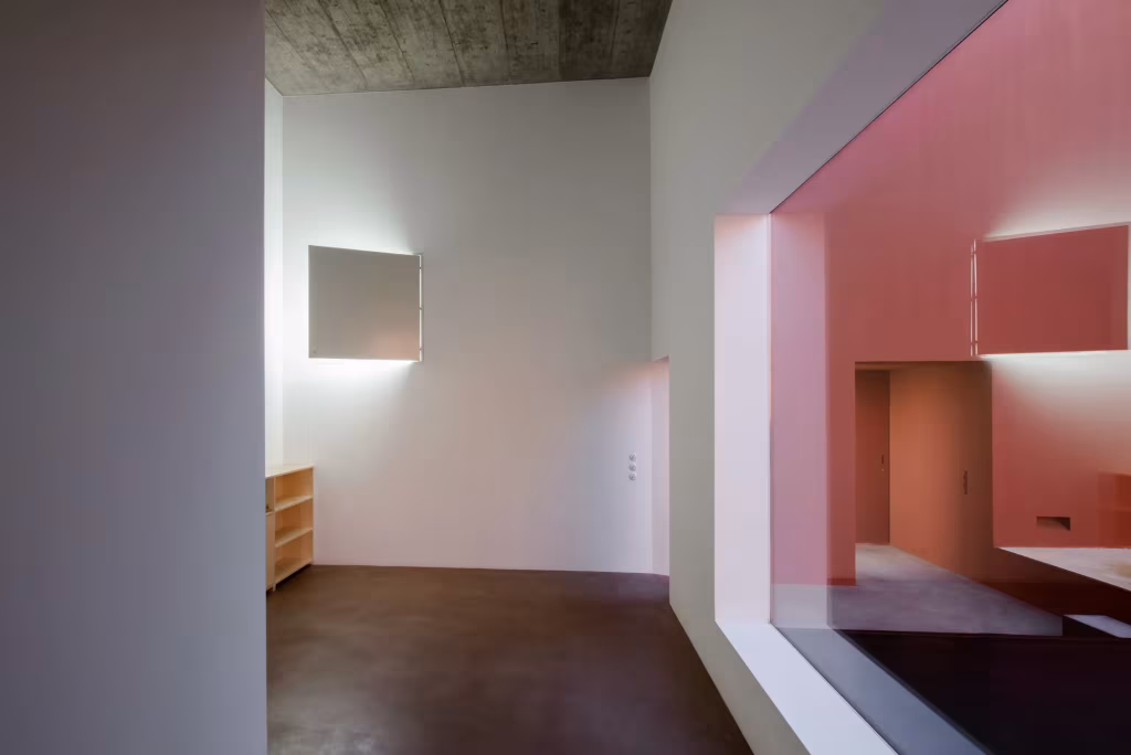Interior blanco con techo de hormigón y un gran hueco hacia un espacio rojo en la Casa en Oeiras