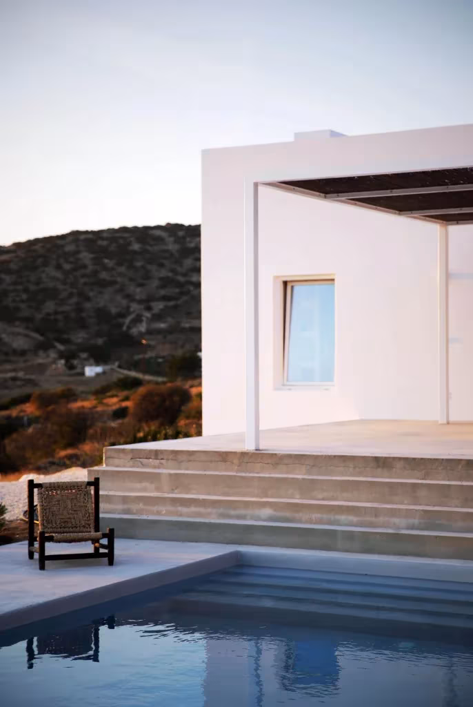 Pórtico con pérgola de la Casa Kamari junto a la piscina, con escalinata y un sillón de madera
