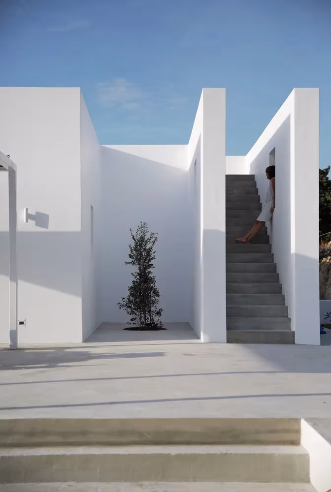Patio entre volúmenes blancos de la Casa Kamari con una escalera exterior que sube a la cubierta
