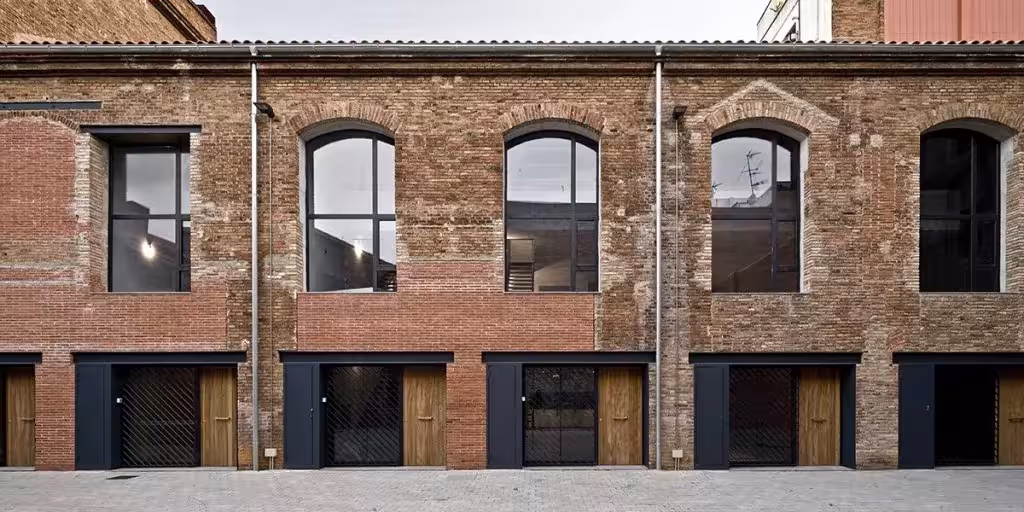 Fachada de ladrillo de la antigua destilería del Poblenou con ventanas en arco y puertas de madera de los lofts