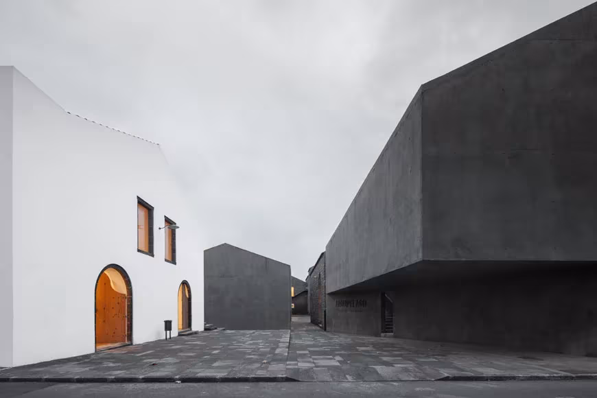 Patio del centro Arquipélago entre la fábrica blanca con puertas en arco y nuevos volúmenes de hormigón oscuro