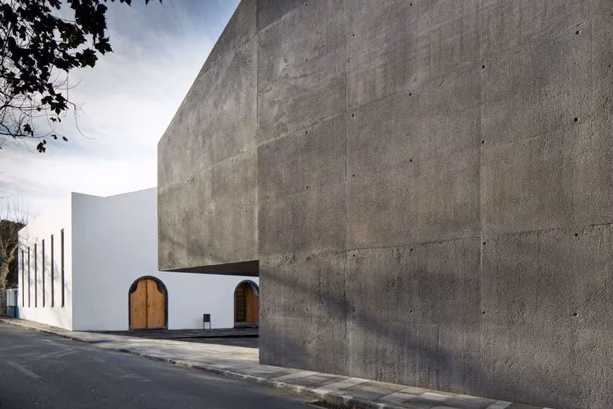 Volumen de hormigón gris del Arquipélago volado junto a un edificio blanco con puertas de madera en arco
