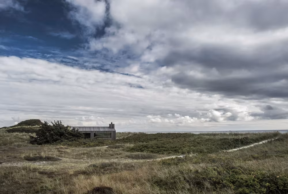 Paisaje de dunas y brezal en Skagen con la Summer Cottage G18 baja en el horizonte bajo nubes