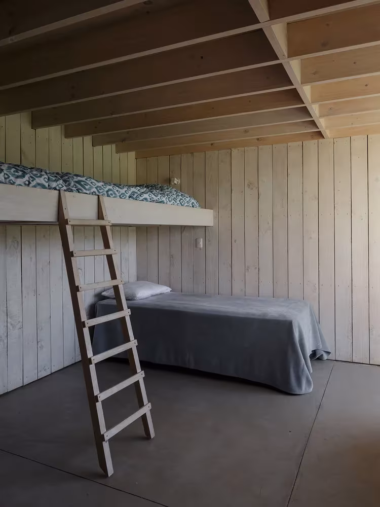 Dormitorio de la Casa CML con altillo de madera, escalera de mano y cama bajo vigas vistas