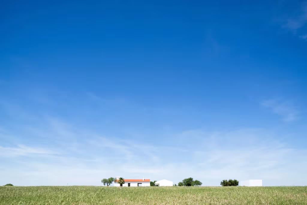 Cielo azul inmenso sobre el campo del Alentejo con el Monte da Azarujinha pequeño en el horizonte