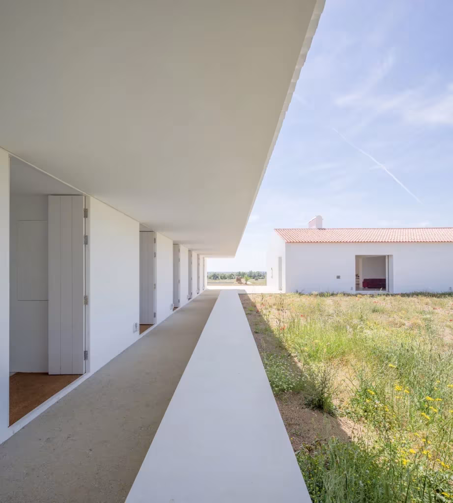 Galería cubierta de Monte da Azarujinha con suelo de hormigón que mira a la casa de tejado rojo
