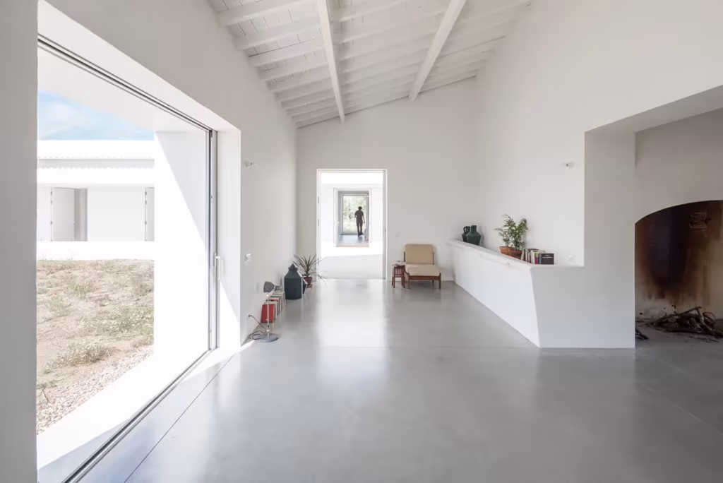 Salón blanco de Monte da Azarujinha con chimenea, gran ventanal y suelo de microcemento gris