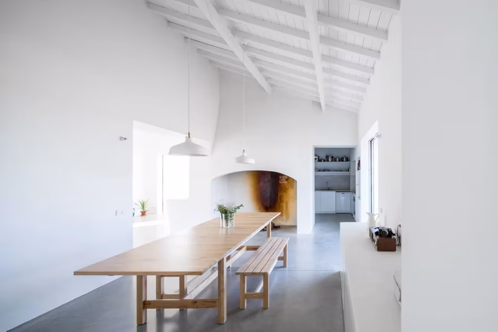 Comedor de Monte da Azarujinha con mesa larga de madera bajo techo de vigas blancas y lámpara colgante