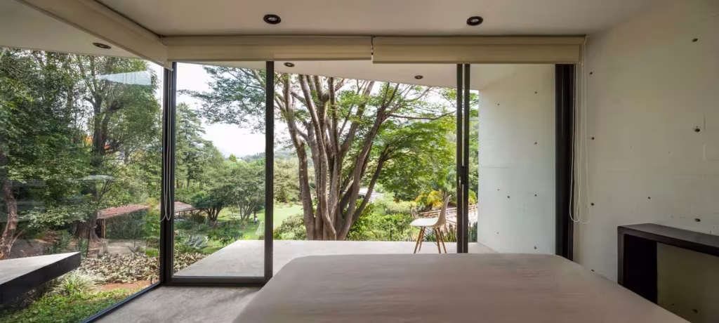 Dormitorio del Bungalow LMM con ventanales de suelo a techo abiertos a los árboles de Tepoztlán