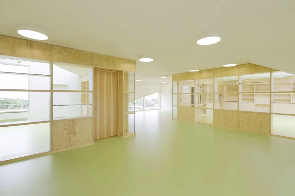 Dorte Mandrup. Guardería infantil Råå. Interior. Iluminación Pasillo interior de la Guardería Råå con suelo verde, tabiques de contrachapado y ventanas al aula