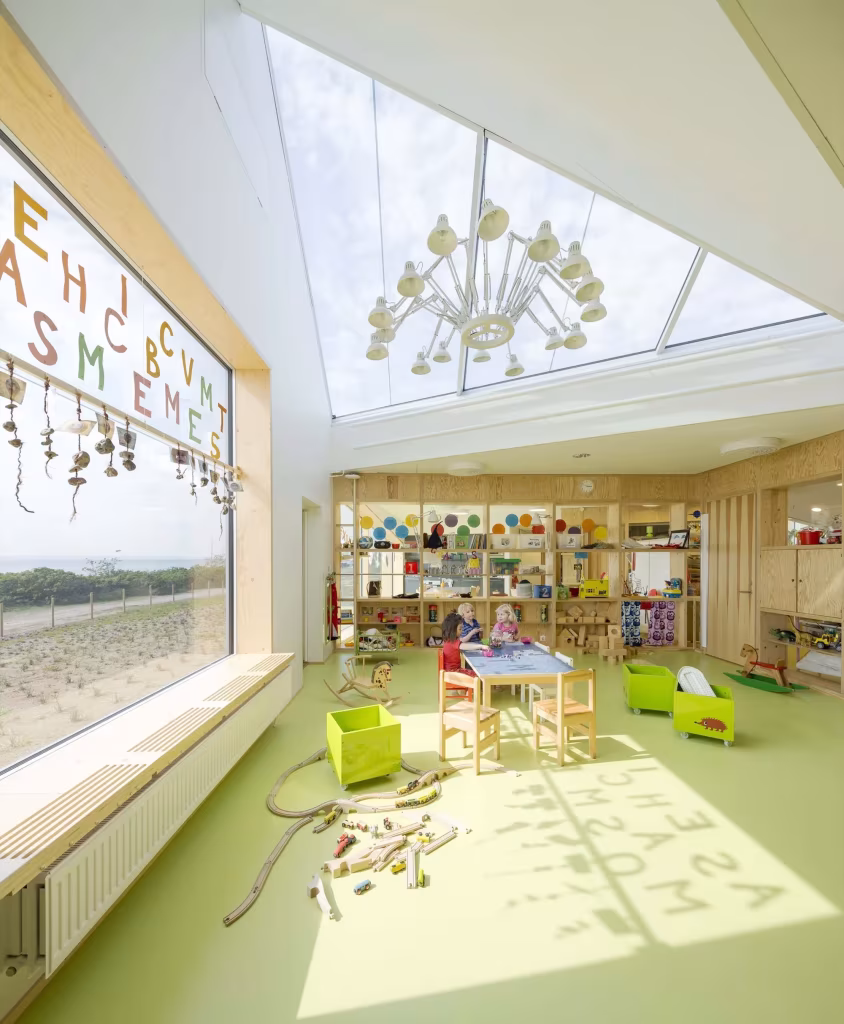 Dorte Mandrup. Guardería infantil Råå. Iluminación. Acristalamiento Aula luminosa de la Guardería Råå con letras en la ventana, mesas infantiles y juguetes de madera