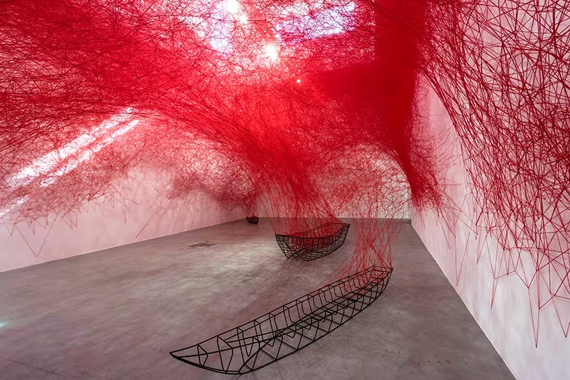 Instalación Uncertain Journey de Chiharu Shiota con hilos rojos que caen sobre armazones metálicos de barcas
