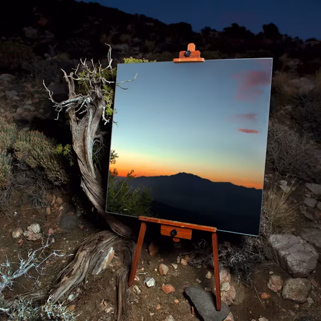 Espejo sobre caballete junto a un tronco seco que refleja el atardecer anaranjado en el desierto
