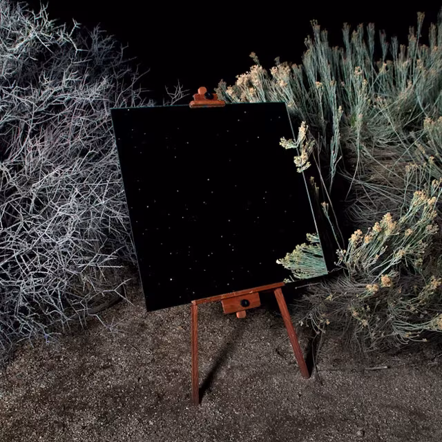 Espejo en caballete de noche entre matorrales del desierto que refleja un cielo estrellado