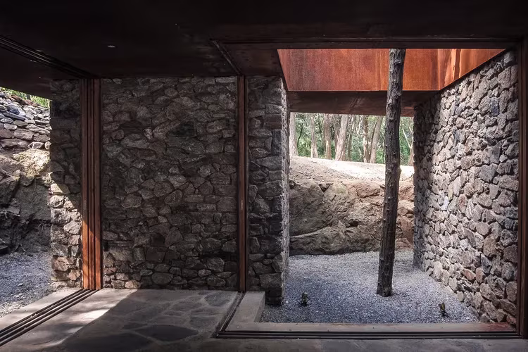 Rockview teahouse arbol integrado en vivienda Interior de la Rockview Teahouse con muros de mampostería, techo de acero corten y un patio con árbol